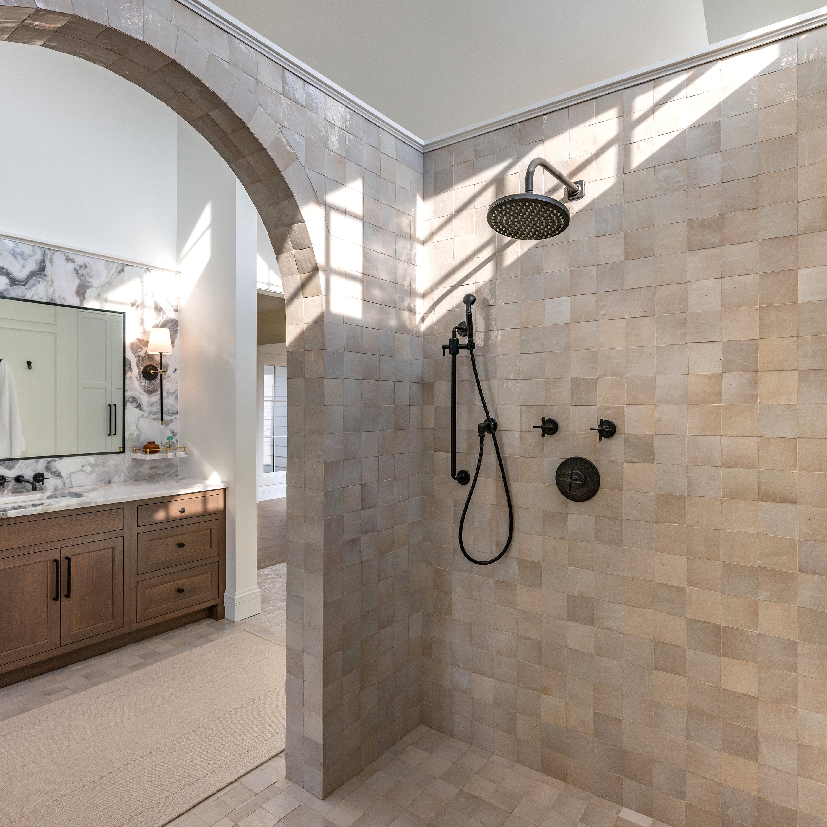 Luxurious bathroom with a walk-in shower, vanity, and large mirror. Off white zellige tile on the floor and walls of the shower.
