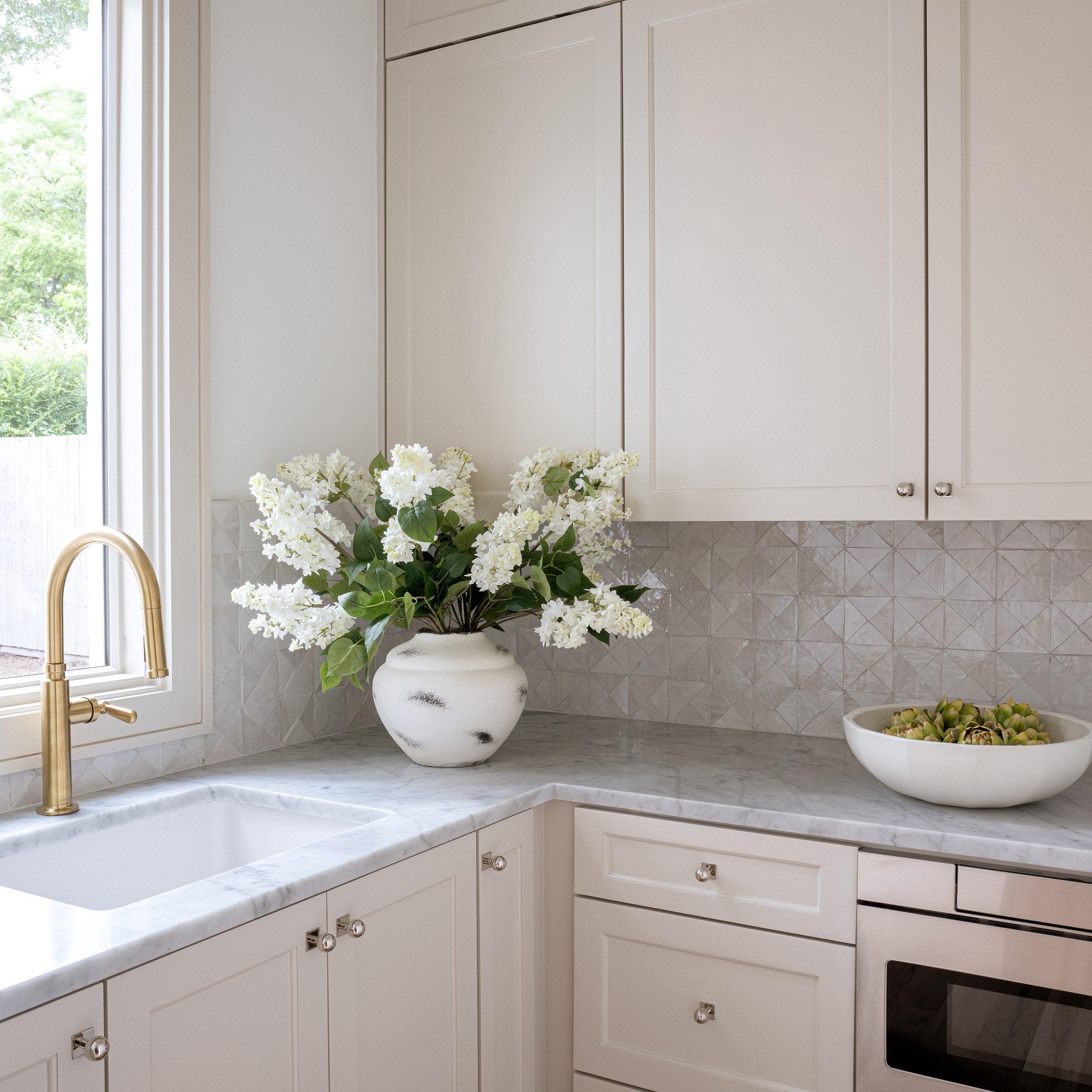 Modern kitchen with white cabinets, gold faucet, and triangle zellige backsplash tile.