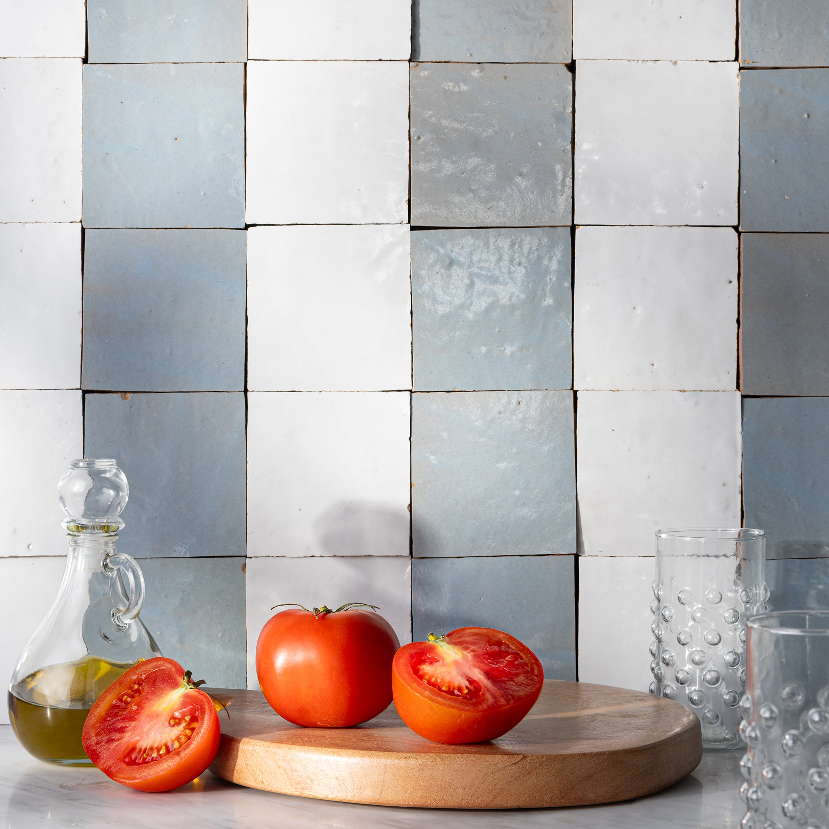 white and blue zellige tile stripe pattern kitchen backsplash with cutting board in front showing tomatoes.