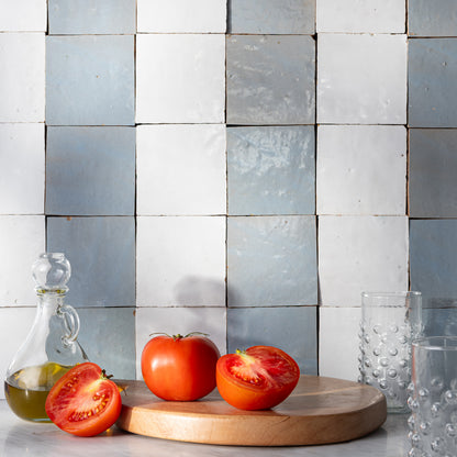 white and blue zellige tile stripe pattern kitchen backsplash with cutting board in front showing tomatoes.