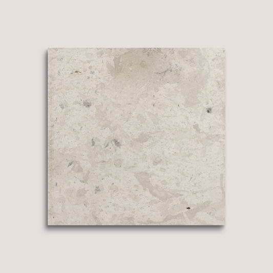 Square limestone tile with a beige and brown speckled pattern on a light gray background