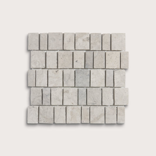 A square mosaic tile sample made of light gray rectangular travertine or marble chips arranged in a staggered brick pattern, shown on a plain light gray background.