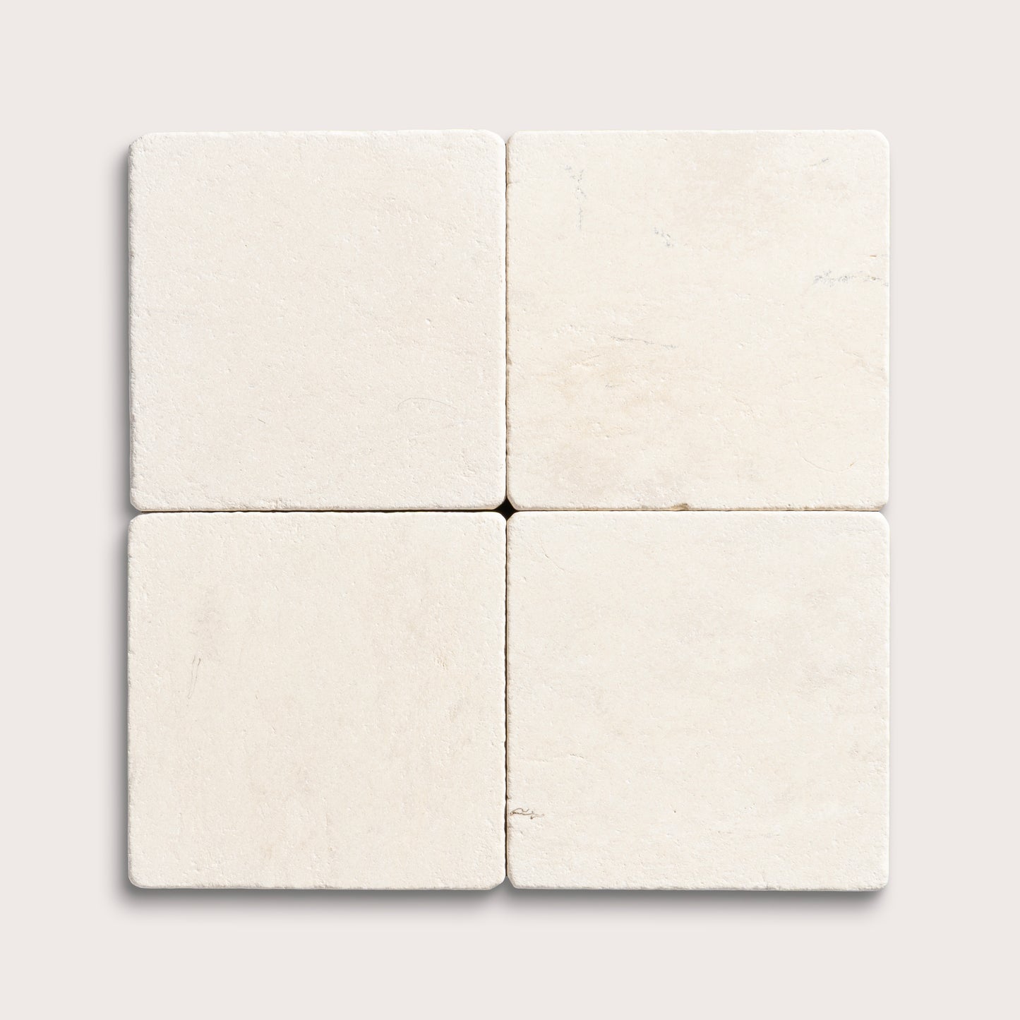 four square tiles with a beige limestone pattern on a white background