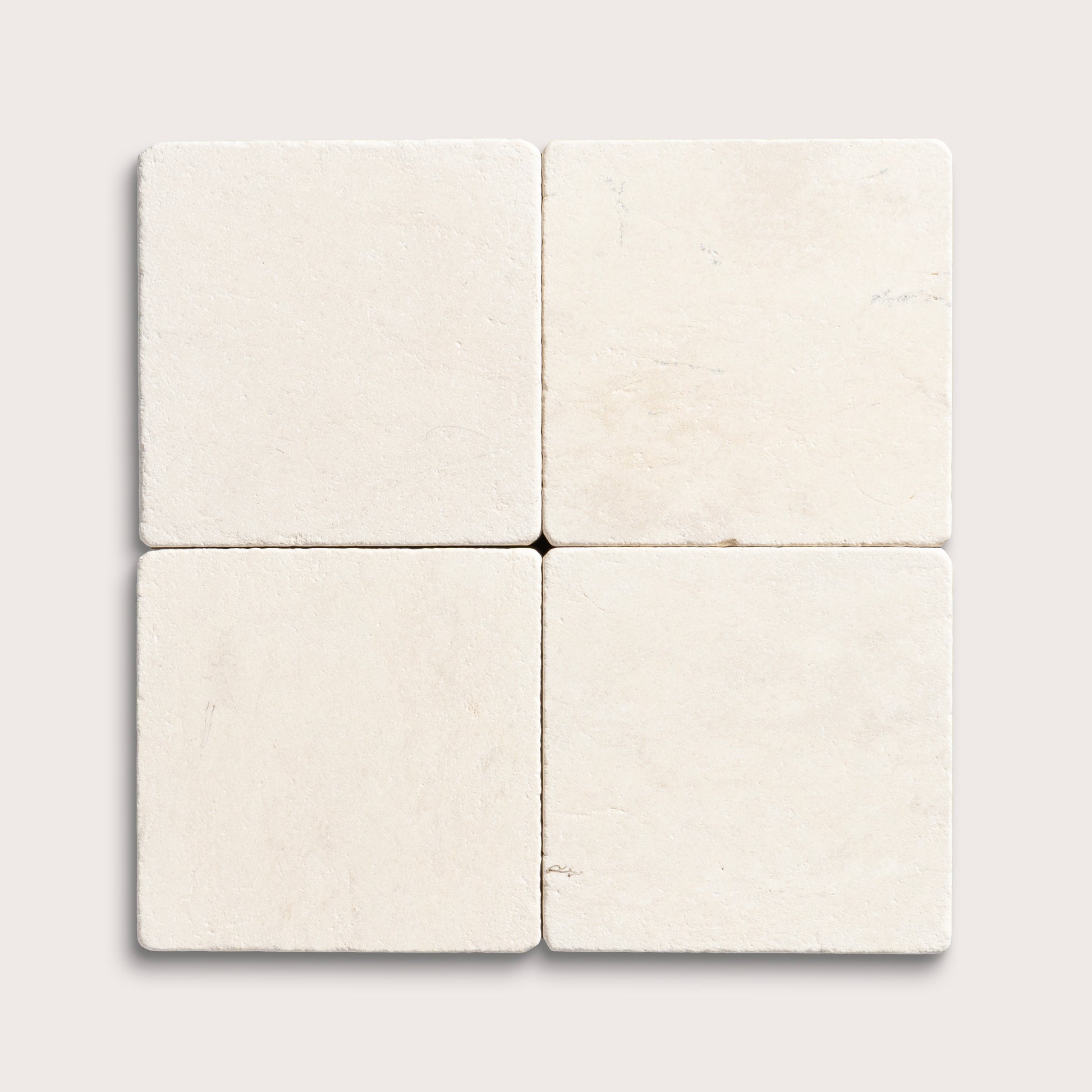four square tiles with a beige limestone pattern on a white background