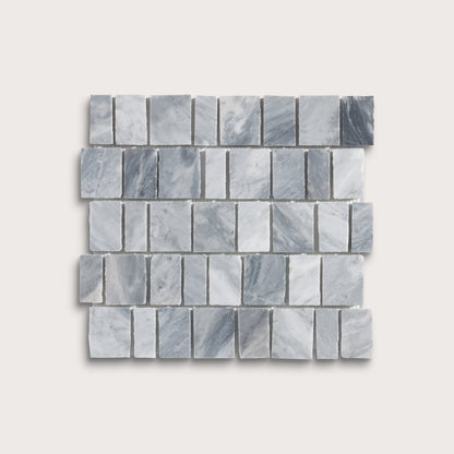A rectangular mosaic tile sample made of small gray marble-like blocks arranged in staggered rows, shown on a light warm gray background.