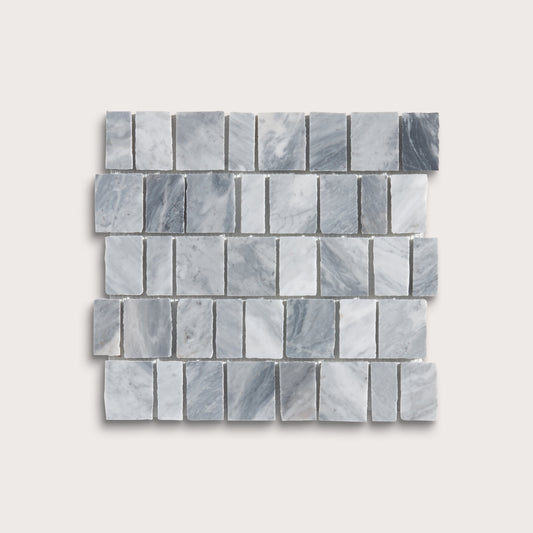 A rectangular mosaic tile sample made of small gray marble-like blocks arranged in staggered rows, shown on a light warm gray background.
