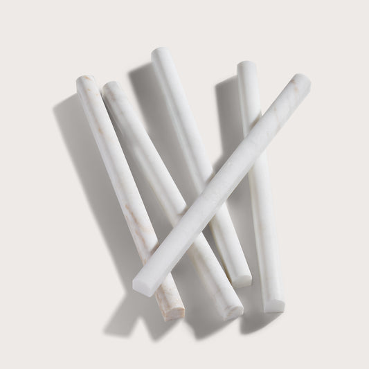 Five white pieces of marble pencil trim arranged in a loose cross pattern on a light beige background with soft shadows.