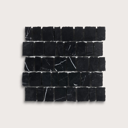 A rectangular arrangement of small black stone tiles with natural white veining, displayed on a light beige background.