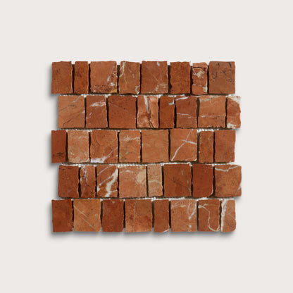 A square mosaic tile sample made of small reddish-brown stone blocks with natural white veining, arranged in a brick pattern on a light gray background.