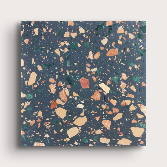 A square sample of terrazzo-style surface material with a dark blue-gray base and scattered multicolored chips in beige, orange, green, and white, shown against a light neutral background.