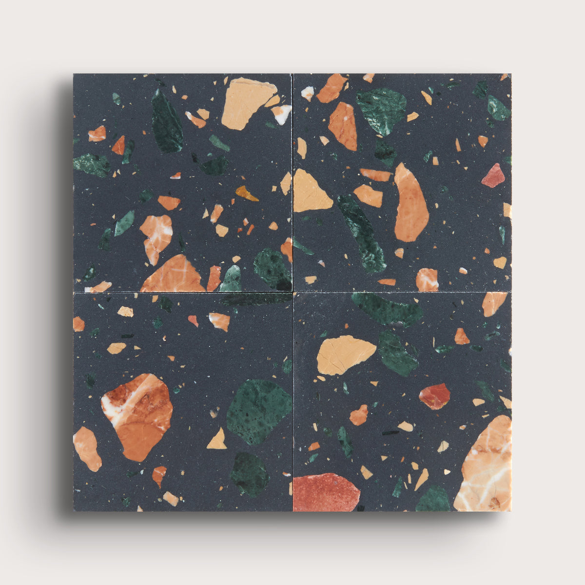 Four square terrazzo-style tiles arranged in a 2x2 grid, featuring a dark charcoal background with scattered orange, green, beige, and rust flecks, shown against a light neutral background.