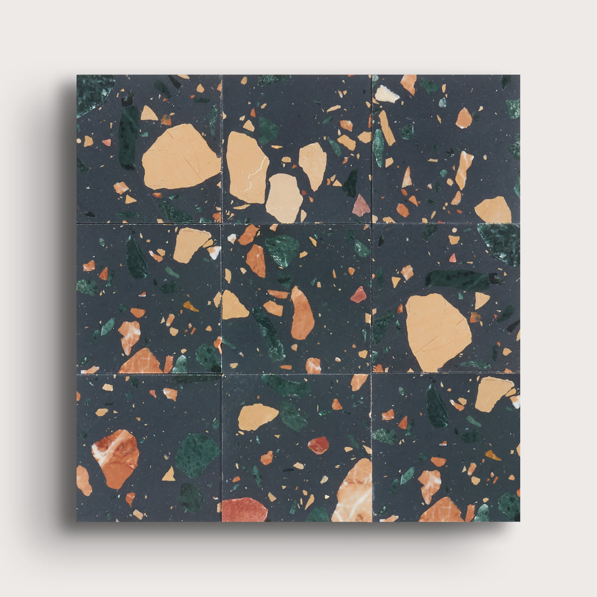 A square terrazzo tile sample or tile sheet with a dark charcoal background and scattered beige, orange, green, and rust flecks, shown against a light gray background.