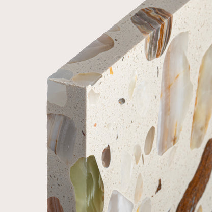 Close-up of a terrazzo slab showing a cream-colored base with embedded natural stone fragments in beige, brown, white, and light green.