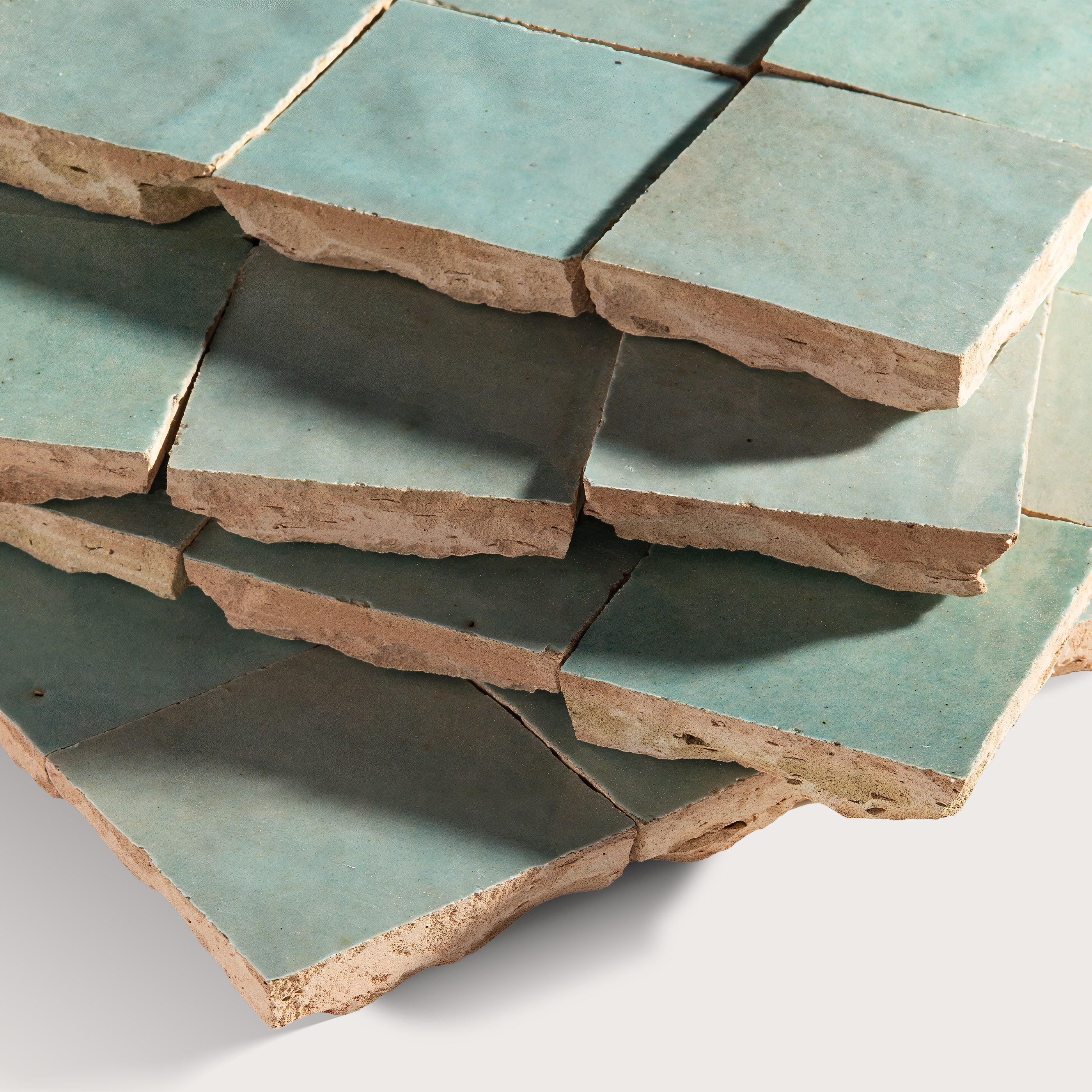 Stack of green zellige tiles with brownish edges on a white background