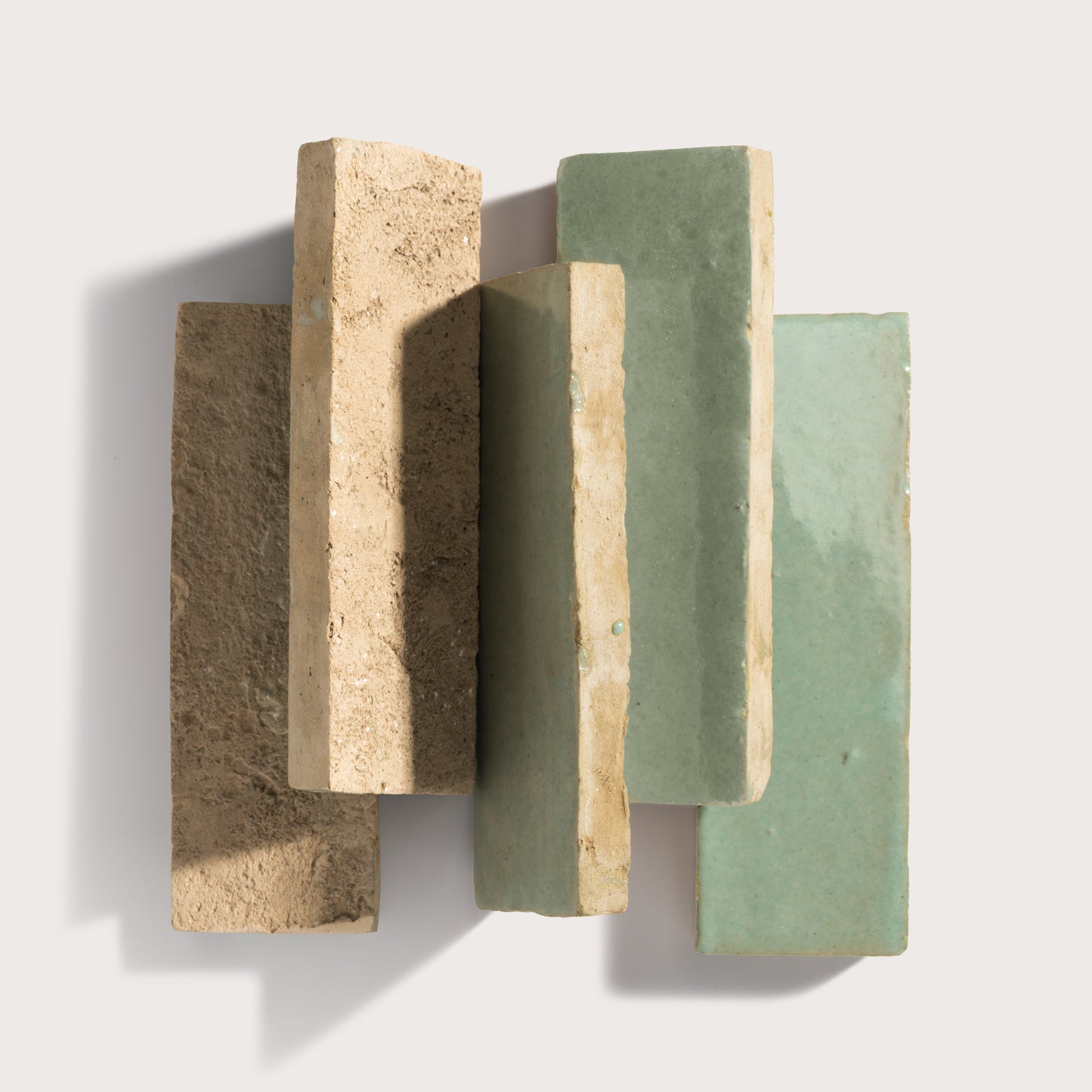Three rectangular zellige tiles in beige, green, and gray on a light gray background