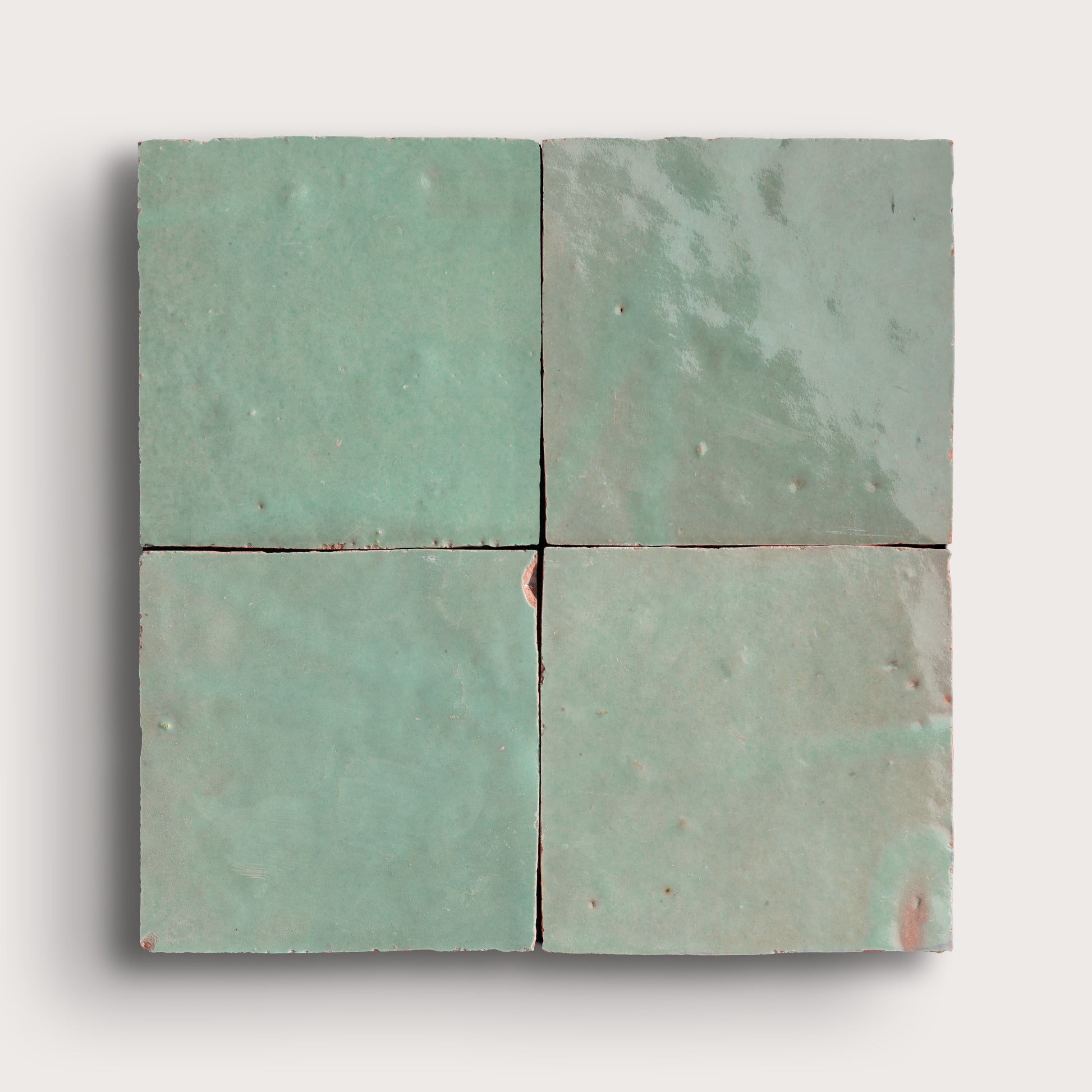 Four square zellige tiles with a greenish-blue pattern on a light gray background