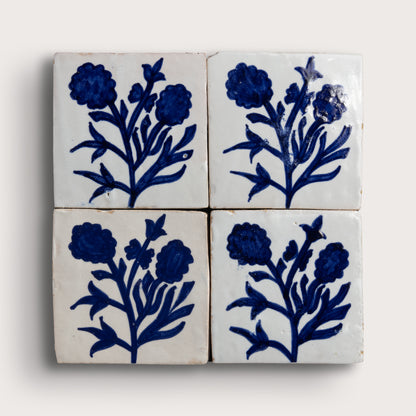 Four square zellige tiles arranged in a 2x2 grid, each decorated with a dark blue floral motif on an off-white background, photographed against a light neutral backdrop.