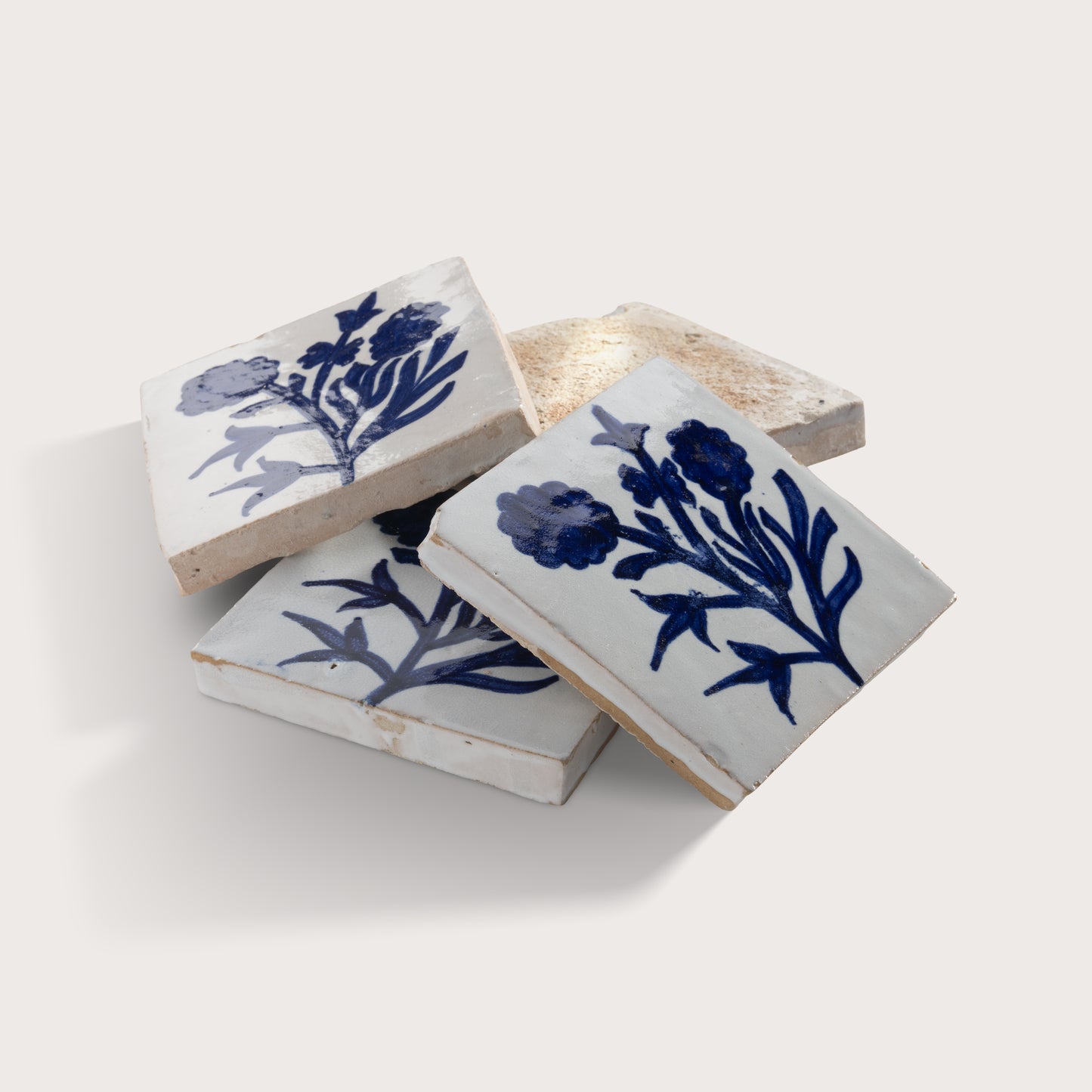 Three square zellige tiles with a white glaze and blue floral pattern, arranged on a light beige background.