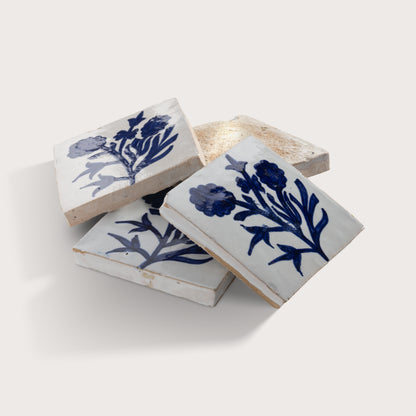 Three square zellige tiles with a white glaze and blue floral pattern, arranged on a light beige background.