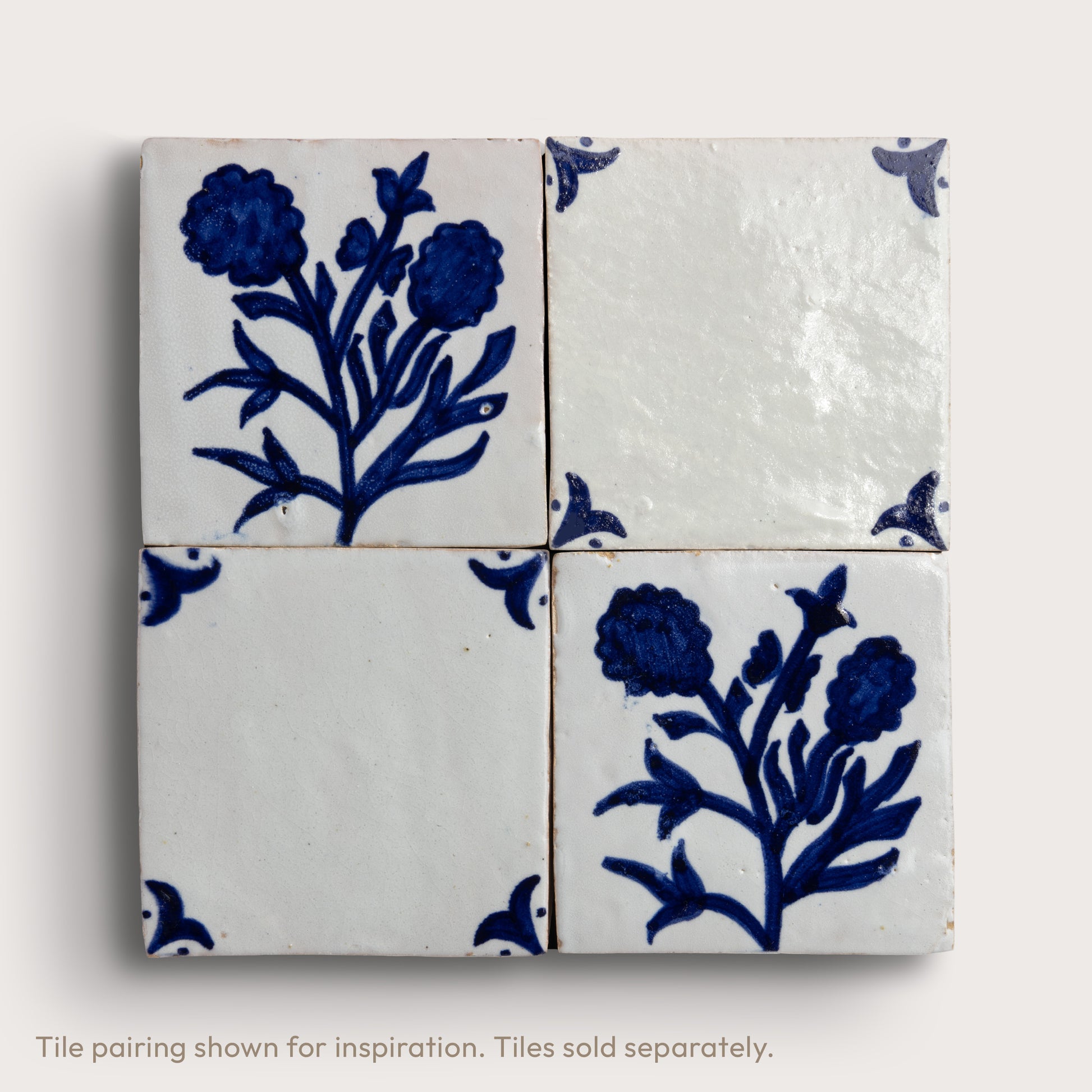 Four square zellige tiles arranged in a 2x2 grid, featuring a blue floral motif on an off-white glazed background, with corner accents on two tiles.