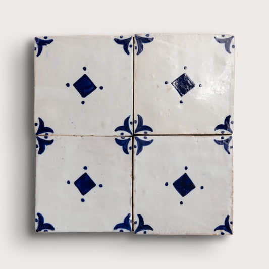 Four square zellige tiles arranged in a 2x2 grid, featuring an off-white glaze with dark blue geometric and floral motifs, shown against a light neutral background.