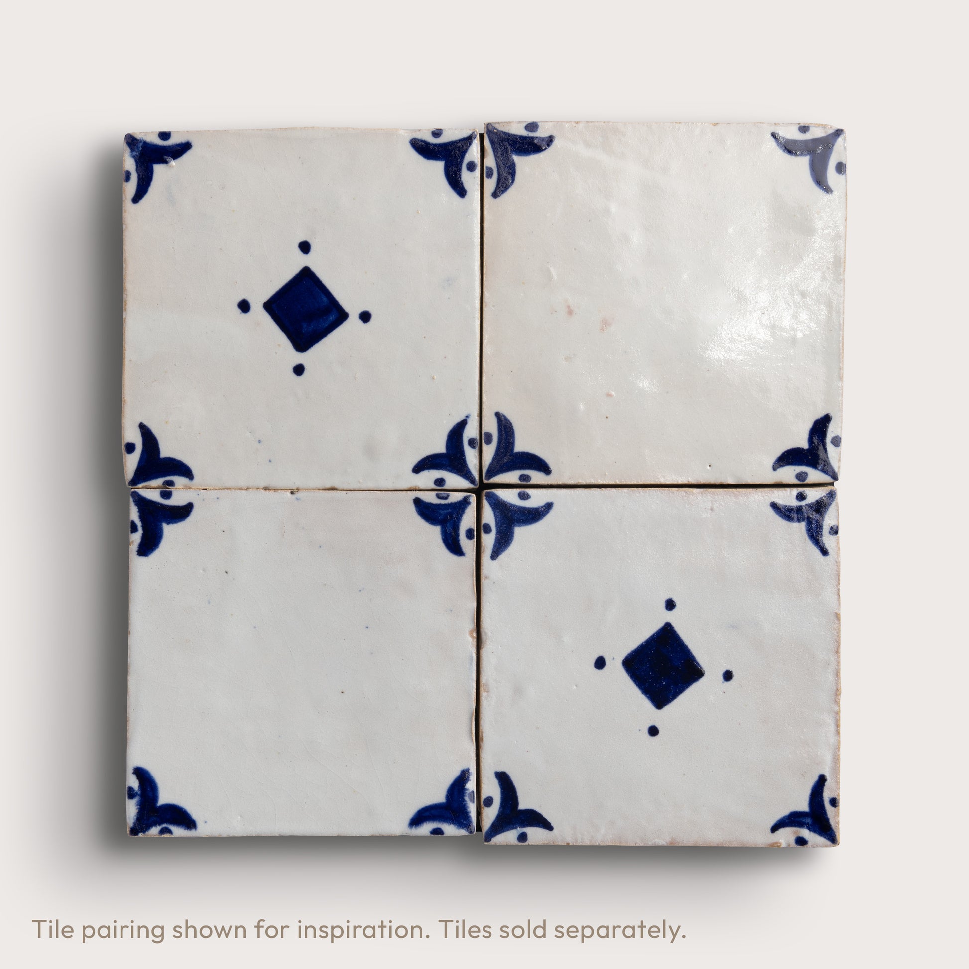 Four square white zellige tiles arranged in a 2x2 grid, featuring a classic Dutch blue pattern with floral motifs and diamond accents, set against a light neutral background.