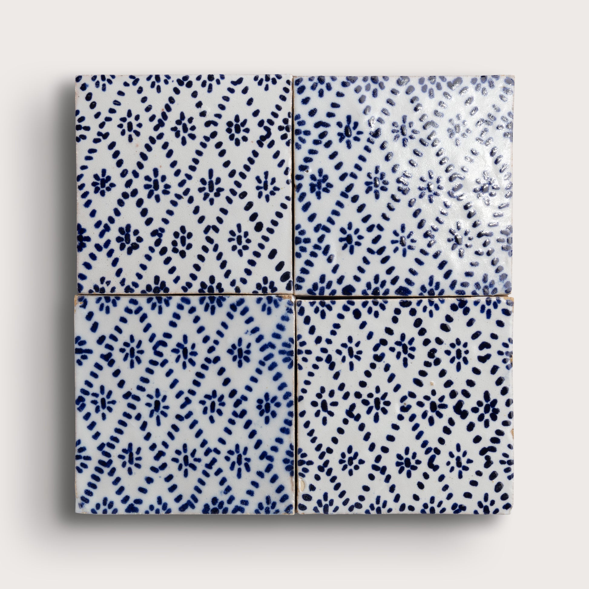 Four square zellige tiles arranged in a 2x2 grid, featuring a blue and white hand-painted floral and geometric pattern on a glossy white glaze, set against a light gray background.