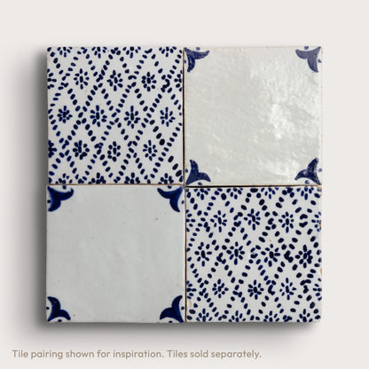 Four square zellige tiles arranged in a 2x2 grid, featuring a mix of solid white, glossy white, and blue hand-painted floral and geometric patterns.