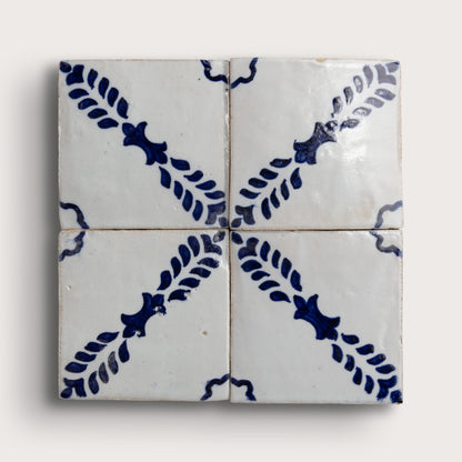 Four square zellige tiles arranged in a 2x2 grid, featuring a white glaze with a dark blue floral and leaf pattern radiating from the center on a light background.
