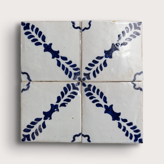 Four square zellige tiles arranged in a 2x2 grid, featuring a white glaze with a dark blue floral and leaf pattern radiating from the center on a light background.