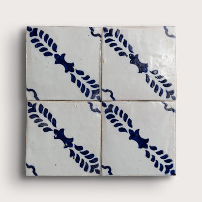 Four square zellige tiles arranged in a 2x2 grid, featuring a white glaze with a dark blue hand-painted diagonal leaf pattern on a light gray background.