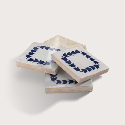 Three square zellige tiles stacked in a fan arrangement, featuring a white glaze with a navy blue leaf border design and a natural beige clay edge.