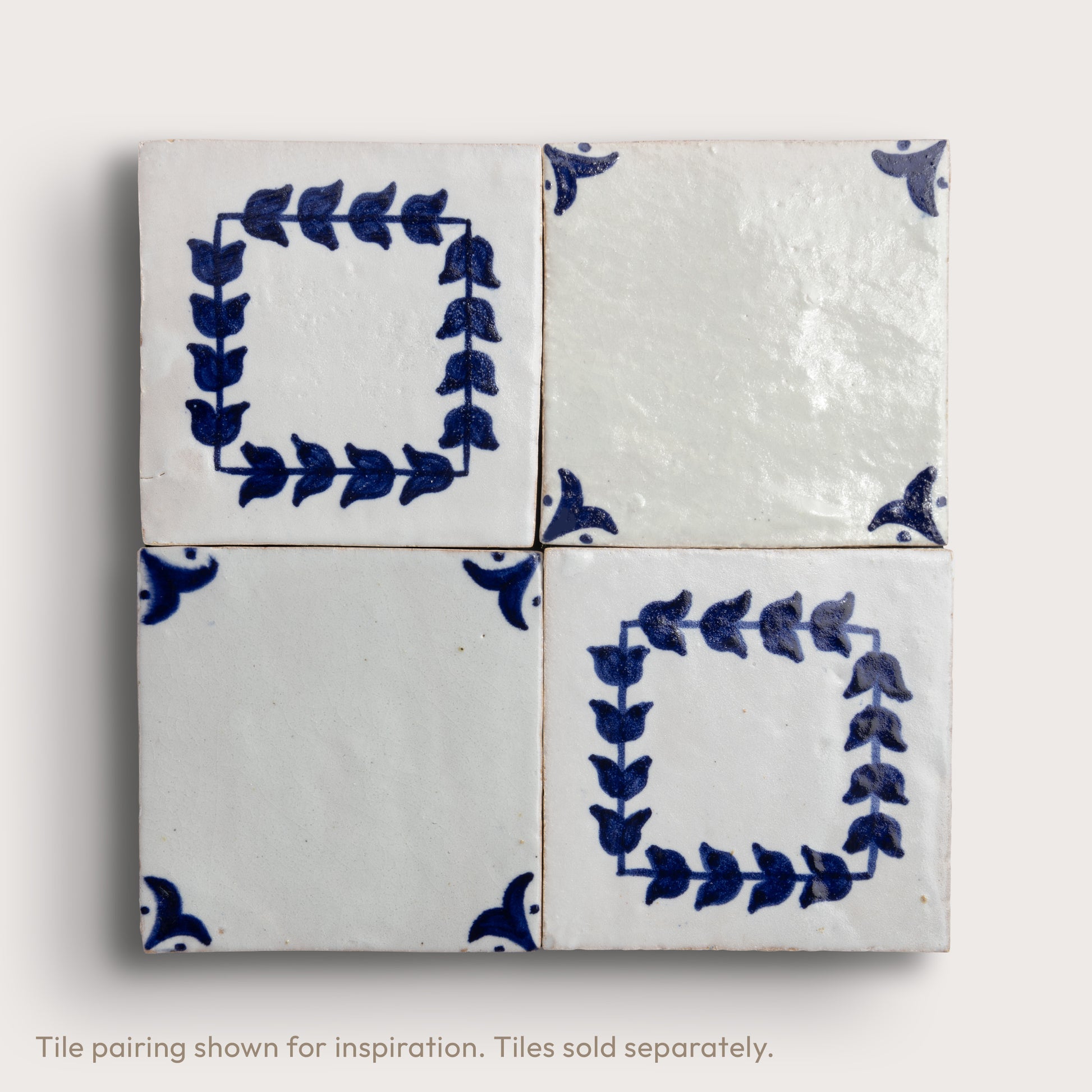 Four square zellige tiles arranged in a 2x2 grid, featuring a white glaze with blue hand-painted floral and leaf motifs, including two leafy square frames and two corner accents.