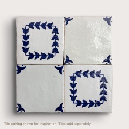 Four square zellige tiles arranged in a 2x2 grid, featuring a white glaze with blue hand-painted floral and leaf motifs, including two leafy square frames and two corner accents.