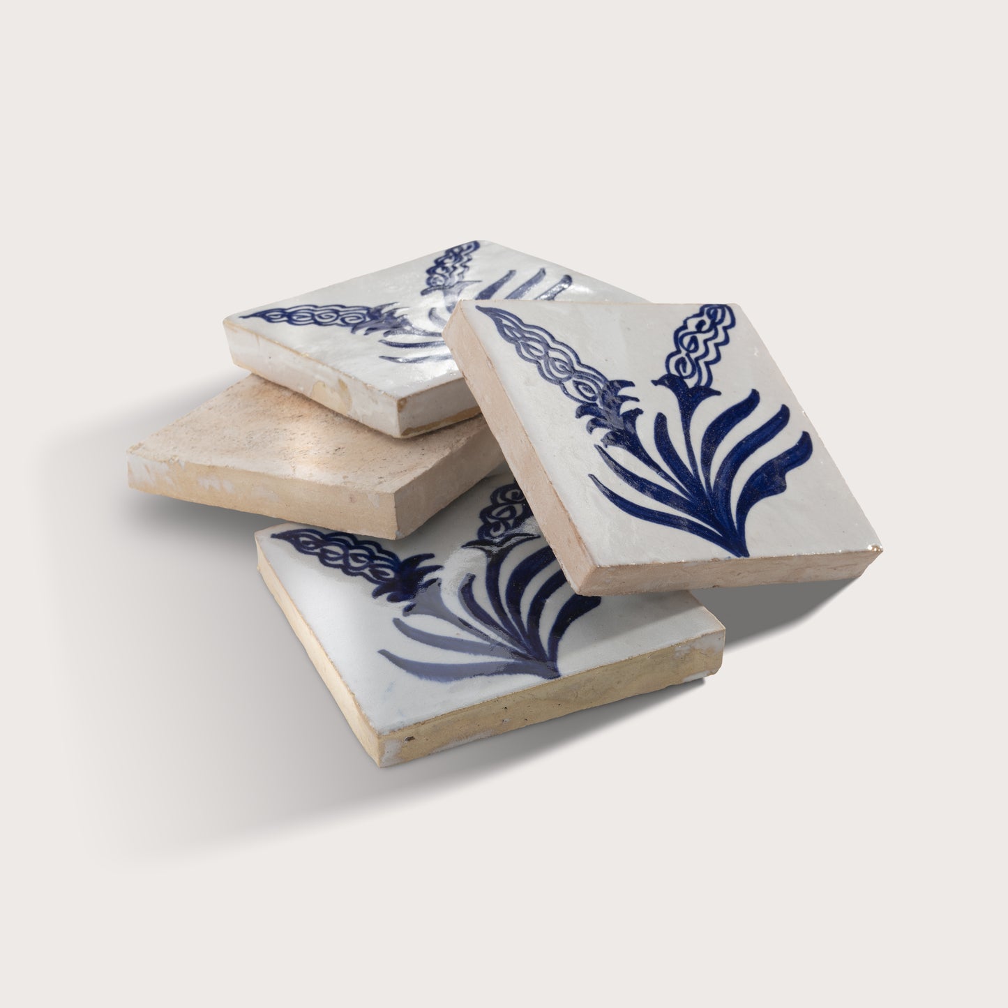 Four square zellige tiles with a white glaze and a blue hand-painted floral pattern, stacked on a light beige background.