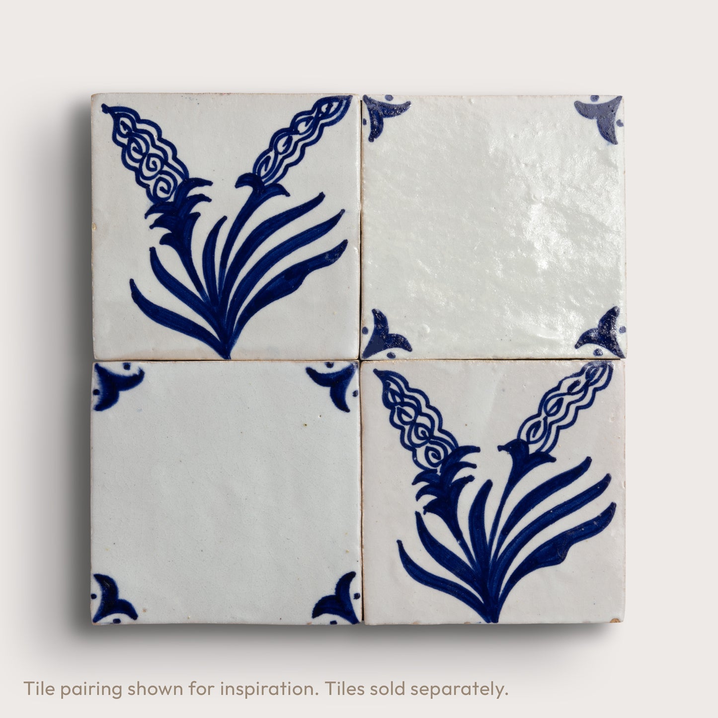 Four square zellige tiles arranged in a 2x2 grid, featuring a white glaze with a dark blue floral and scroll pattern, set against a light neutral background.