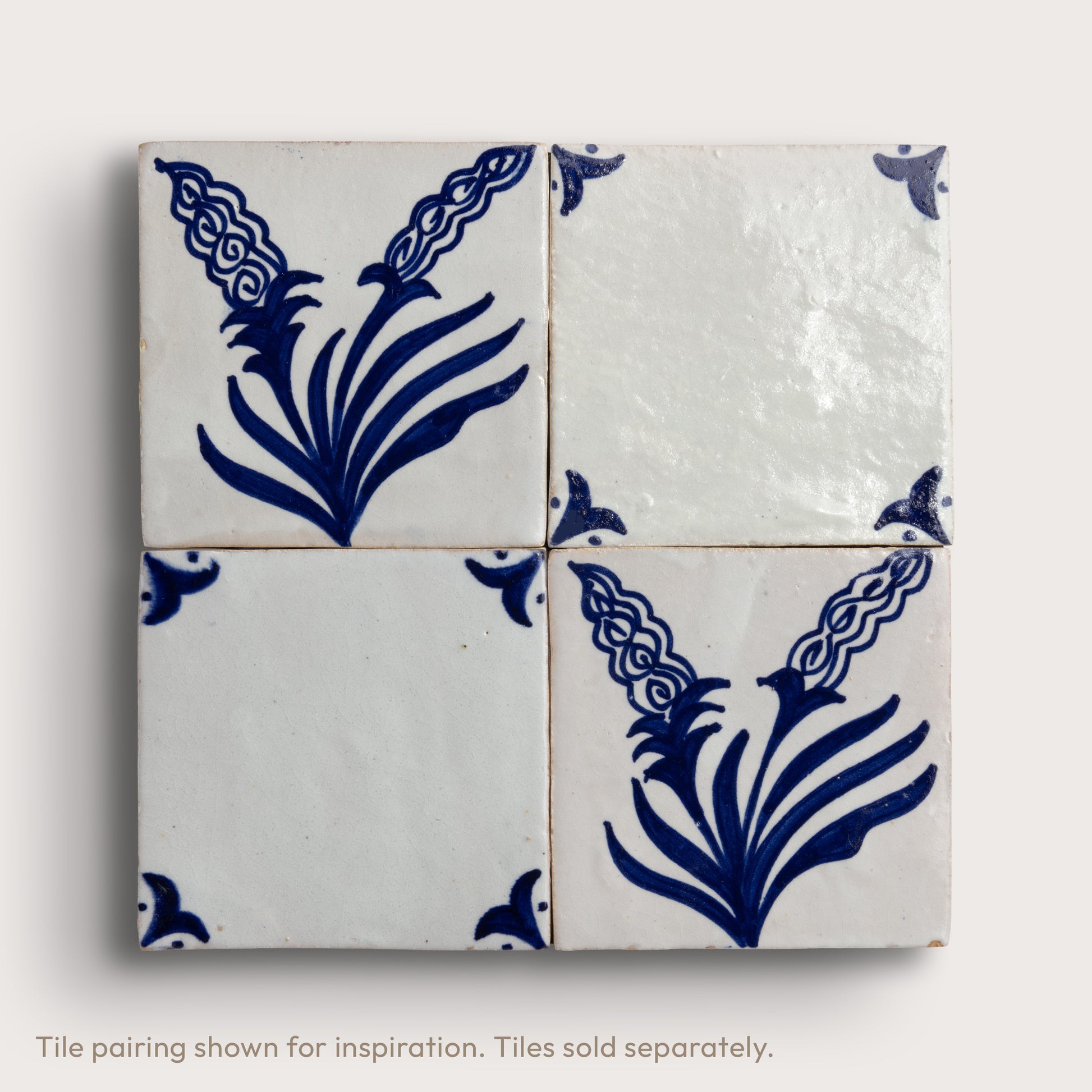 Four square zellige tiles arranged in a 2x2 grid, featuring a white glaze with a dark blue floral and scroll pattern, set against a light neutral background.
