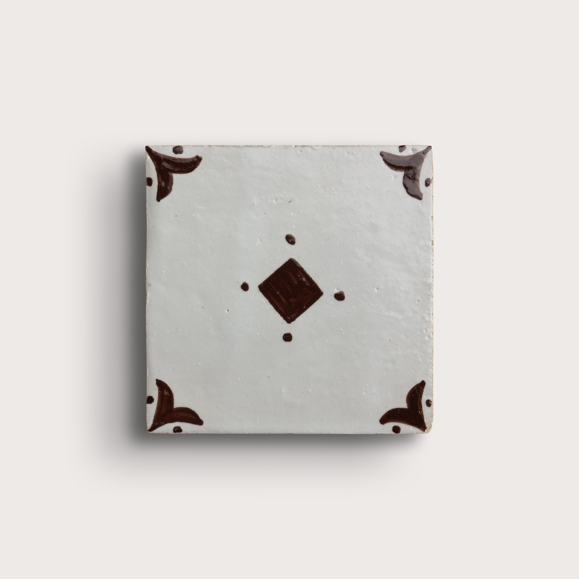 A square zellige tile with a light gray glaze, featuring a central dark brown diamond motif and matching dark brown corner flourishes, shown on a light beige background.