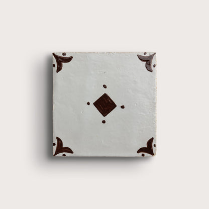 A square zellige tile with a light gray glaze, featuring a central dark brown diamond motif and matching dark brown corner flourishes, shown on a light beige background.