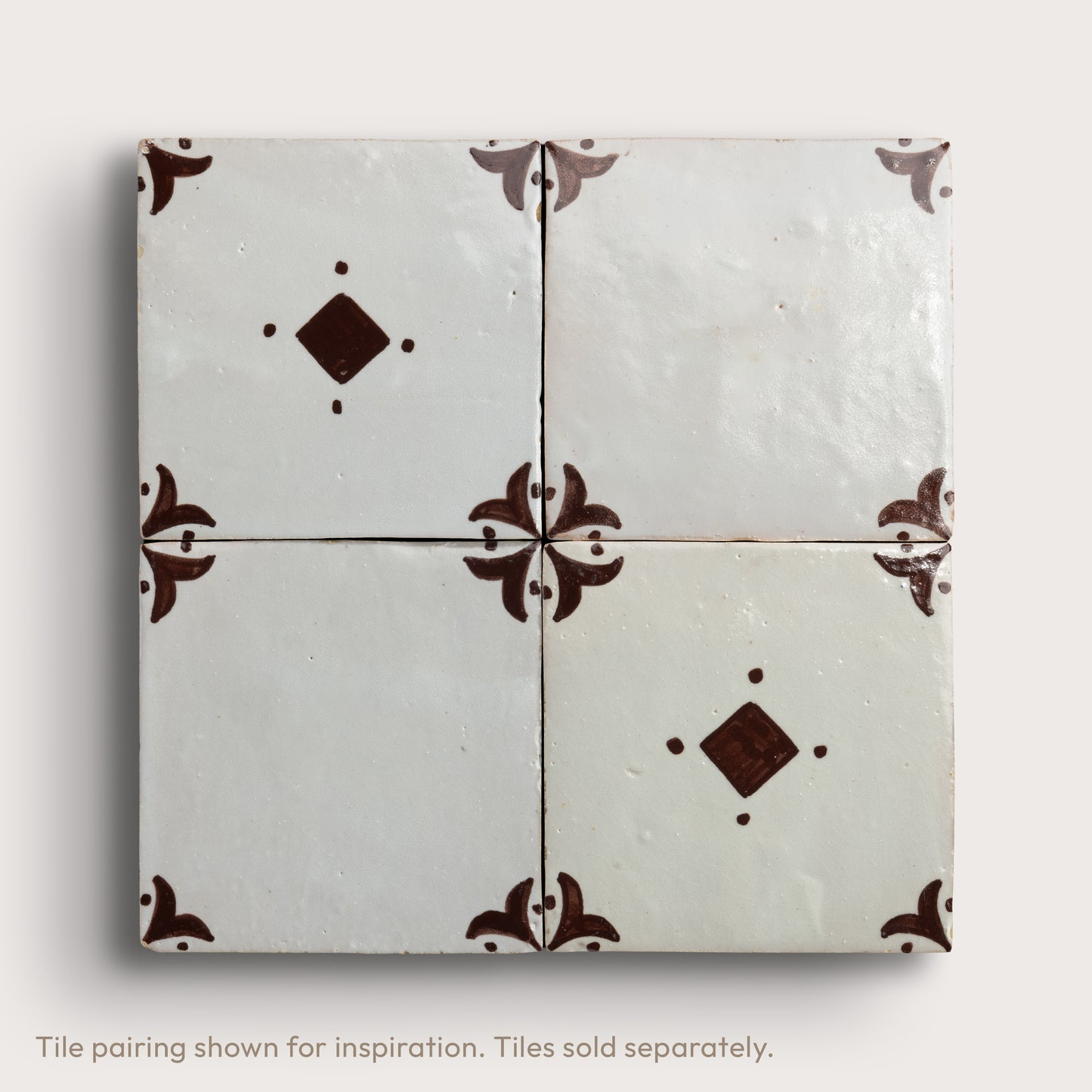 Four square zellige tiles arranged in a 2x2 grid, featuring a glossy off-white glaze with dark brown decorative floral corner motifs and diamond accents, set against a light neutral background.
