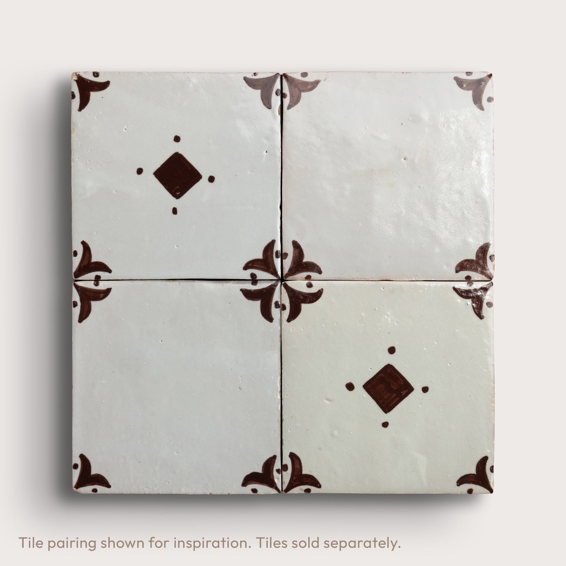 Four square zellige tiles arranged in a 2x2 grid, featuring a glossy off-white glaze with dark brown decorative floral corner motifs and diamond accents, set against a light neutral background.