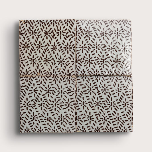 Four square zellige tiles in a grid pattern on a light gray background. Two tiles feature a brown hand-painted abstract brushstroke pattern on a white glaze, while the bottom tile shows a textured, unglazed beige clay surface.