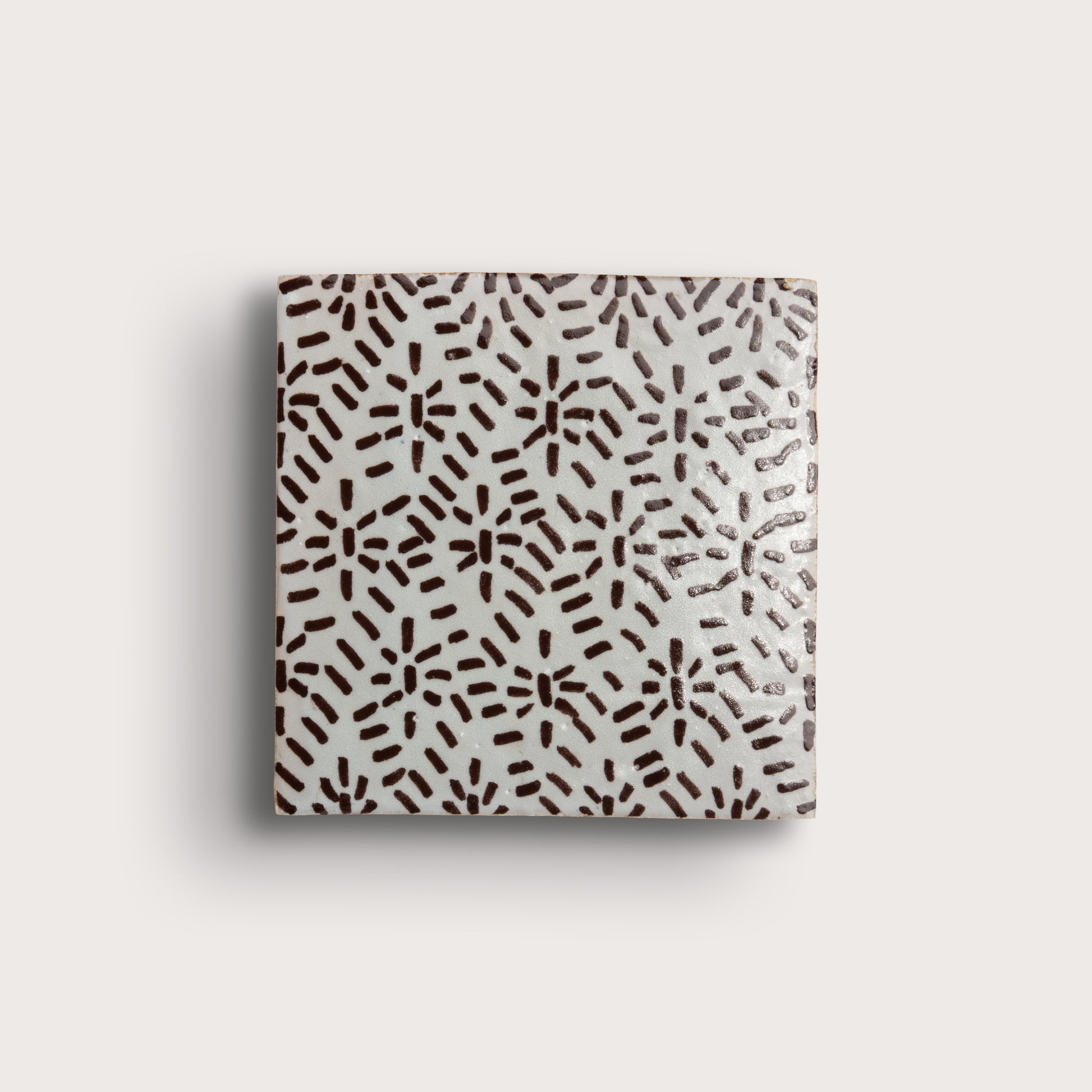 square zellige tile on a light gray background. brown hand-painted abstract brushstroke pattern on a white glaze.