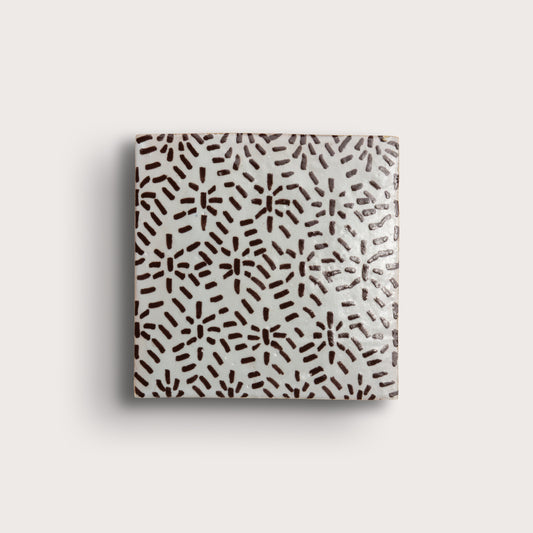 square zellige tile on a light gray background. brown hand-painted abstract brushstroke pattern on a white glaze.