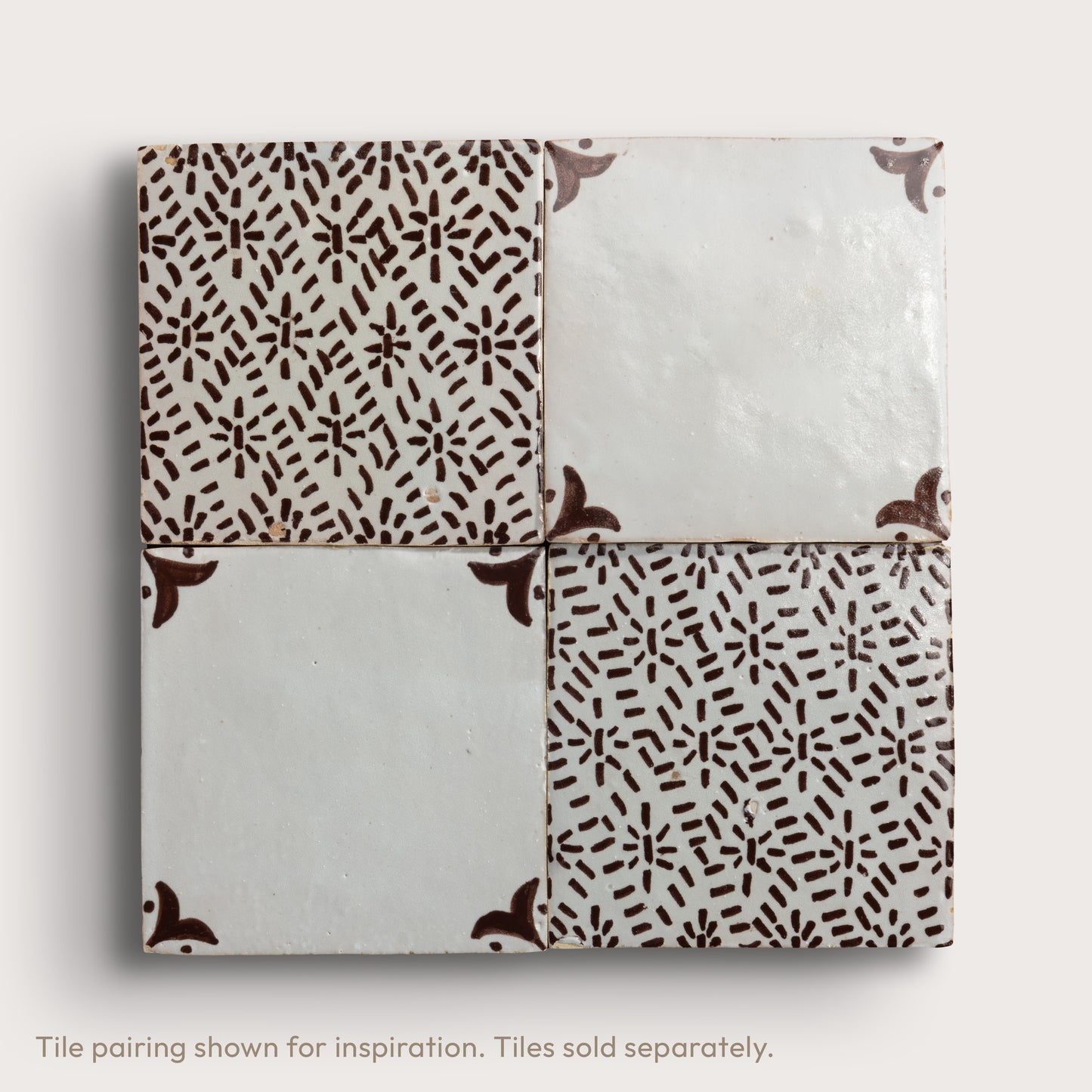 Four square zellige tiles in a grid pattern on a light gray background. Two tiles feature a brown hand-painted abstract brushstroke pattern on a white glaze, while the bottom tile shows a textured, unglazed beige clay surface.