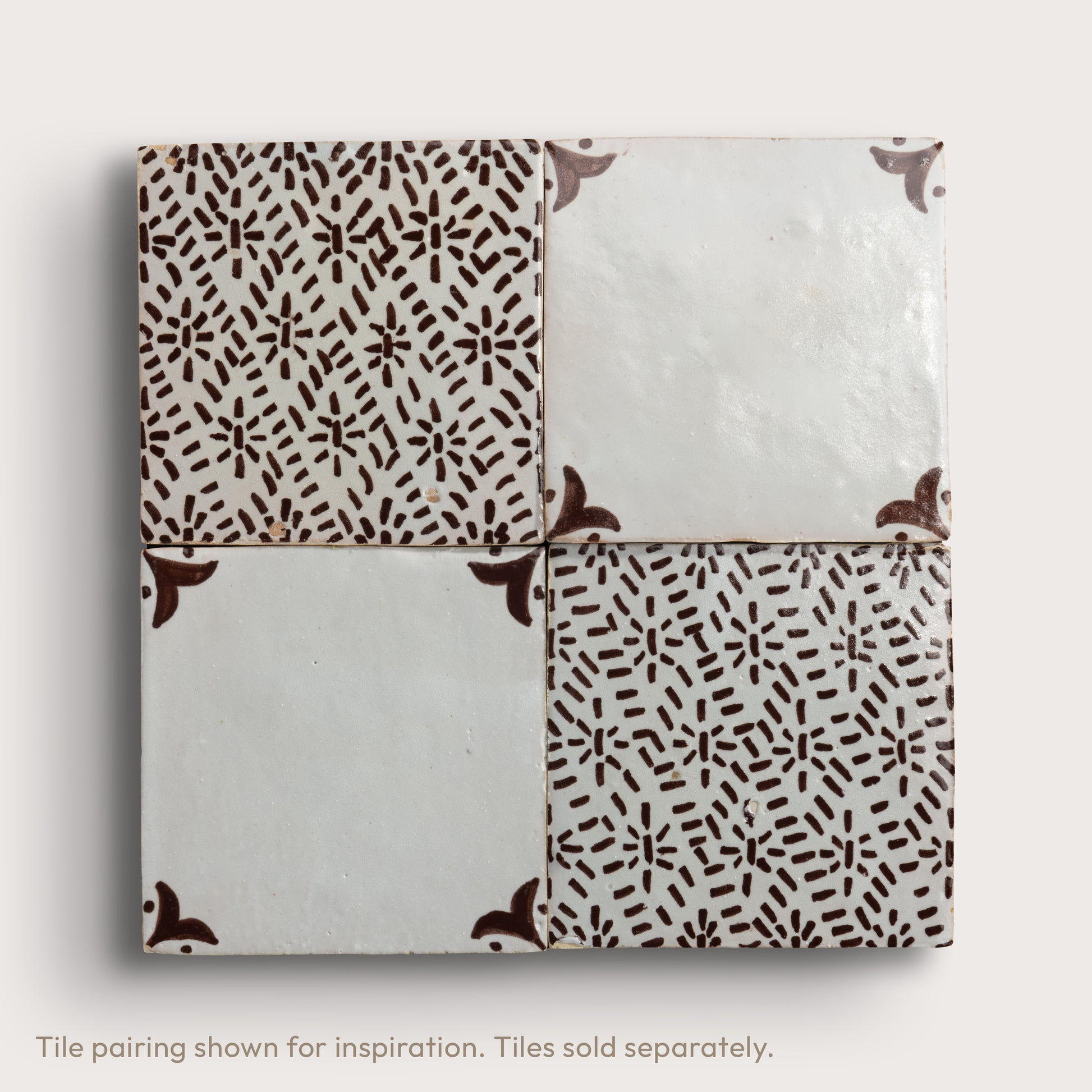 Four square zellige tiles in a grid pattern on a light gray background. Two tiles feature a brown hand-painted abstract brushstroke pattern on a white glaze, while the bottom tile shows a textured, unglazed beige clay surface.