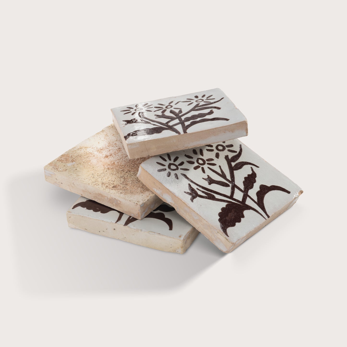 four square zellige tiles stacked on a light gray background. Brown hand painted designs.