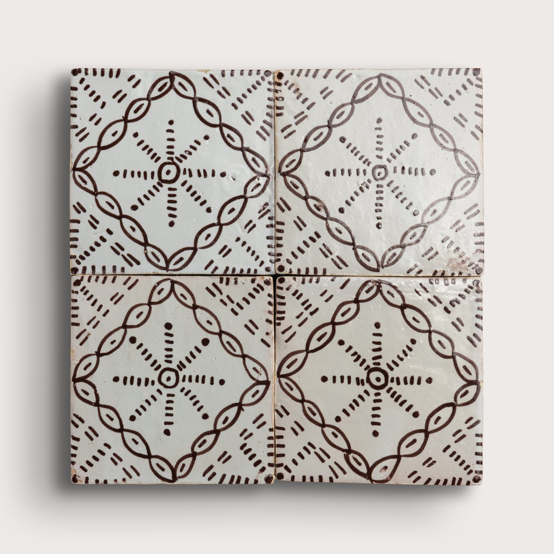 square zellige tile in a grid format with a handpainted brown pattern shot on a light gray background.