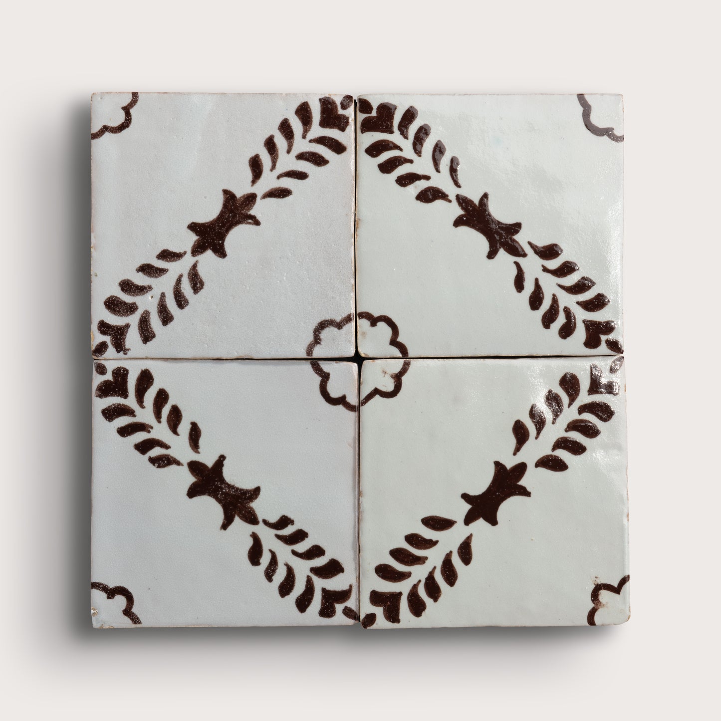 Four square zellige tiles arranged in a 2x2 grid, featuring a glossy off-white glaze with a dark brown hand-painted botanical pattern of leafy stems and star-like motifs.