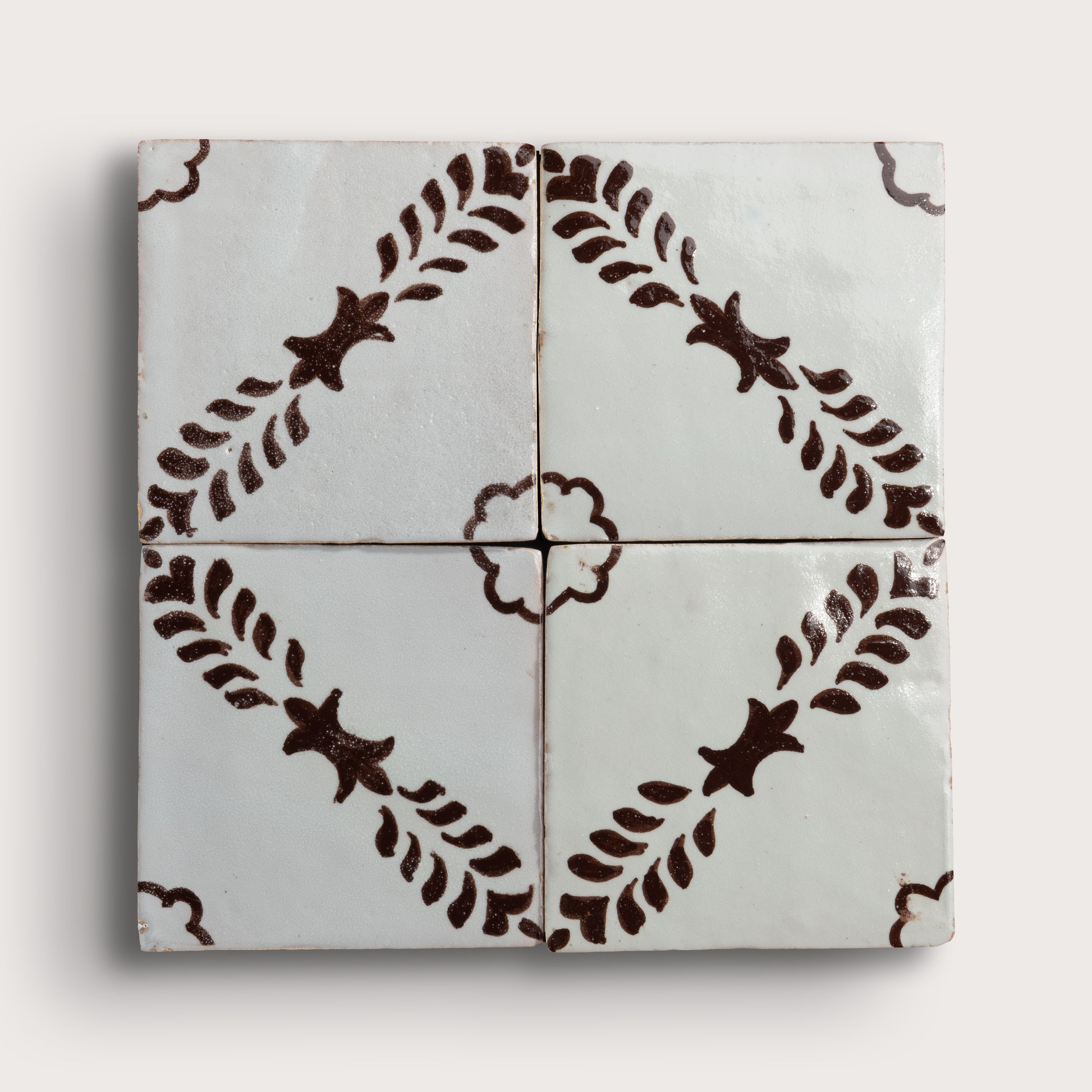 Four square zellige tiles arranged in a 2x2 grid, featuring a glossy off-white glaze with a dark brown hand-painted botanical pattern of leafy stems and star-like motifs.